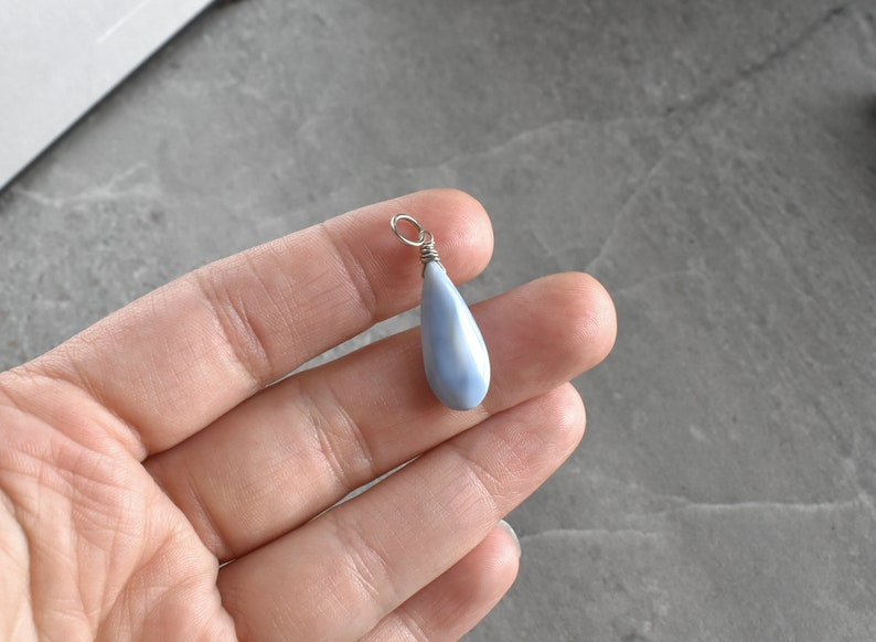May include: A teardrop-shaped pendant made of blue opal with a silver wire wrap. The pendant is hanging from a silver chain.