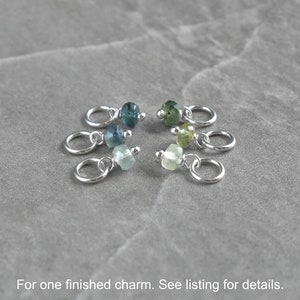 Op de afbeelding: Zes zilveren bedels met verschillende gekleurde edelsteen kralen. De kralen zijn in tinten blauw en groen. De bedels zijn voor het maken van sieraden.