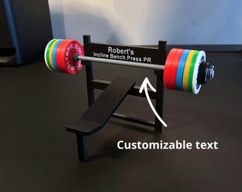 May include: A miniature black weight bench with a barbell featuring colorful weight plates. The barbell has the text "Robert's Incline Bench Press PR" on the sign. The image also includes the text "Customizable text".
