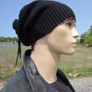 May include: A black knit beanie with a long, thin string hanging from the back. The beanie is pulled down low on the forehead, and the string is tied in a knot at the back of the head.