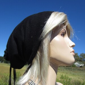 May include: A black beanie with long ties, worn by a mannequin with long, blonde hair and a silver beaded fringe necklace.