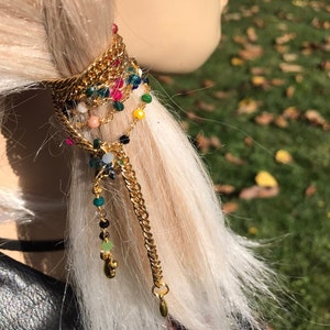 May include: Gold chain hair tie with colorful beads and charms. The chain is wrapped around a ponytail and has a dangling charm at the end.