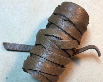 May include: A roll of brown leather cord, approximately 1/2 inch wide, is coiled and ready for crafting projects.