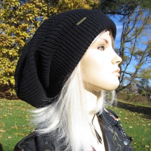 Peut inclure: Un béret noir en tricot avec une étiquette dorée. Le béret est porté par une personne aux cheveux longs et blancs et une veste en cuir noir avec des broderies florales.