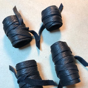 May include: Four black leather cord wraps, each with a different length and width, are arranged on a brown surface.