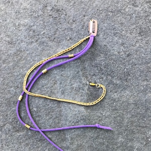 May include: Purple suede cords with gold chain and beads, attached to a gold hair clip.