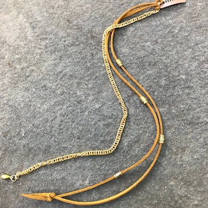 May include: A gold chain necklace with a brown leather cord and gold beads. The necklace has a gold clip at the top.