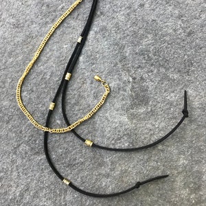 May include: A black hair clip with two black cords attached. The cords have gold beads and a gold chain attached to the clip.
