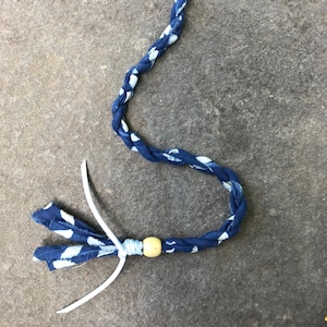 May include: A blue and white braided fabric hair tie with a wooden bead and a black plastic clip.
