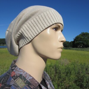 May include: A beige knitted beanie with a slouchy fit. The beanie is made of a soft, comfortable material and has a ribbed texture.