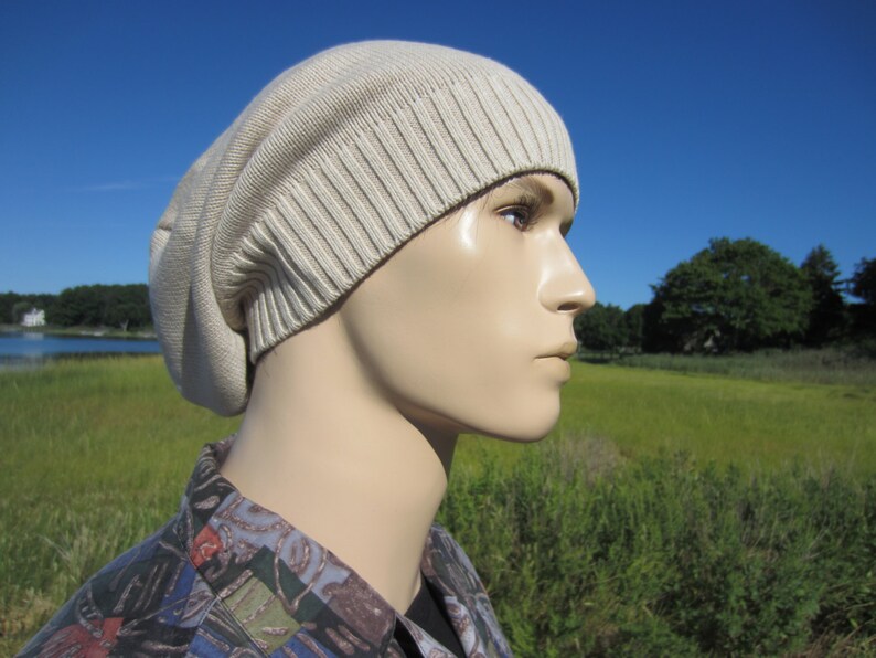 May include: A beige knitted beanie with a slouchy fit. The beanie is made of a soft, comfortable material and has a ribbed texture.