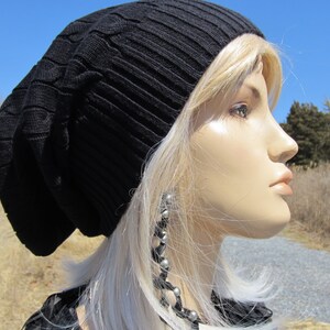 Puede incluir: Un gorro negro de punto con un patr&oacute;n de trenza. El gorro lo lleva una persona con el pelo largo y rubio y pendientes de plata.