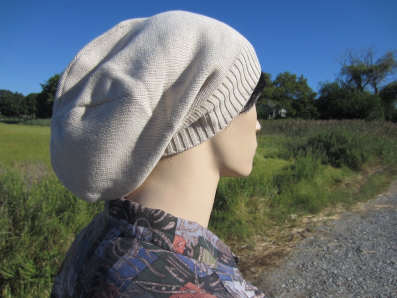 May include: A beige slouchy beanie with a ribbed brim. The beanie is made of a soft, knitted fabric.
