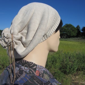 May include: A beige slouchy beanie with a brown leather tie. The beanie is made of a soft, knitted fabric and has a relaxed, casual look.