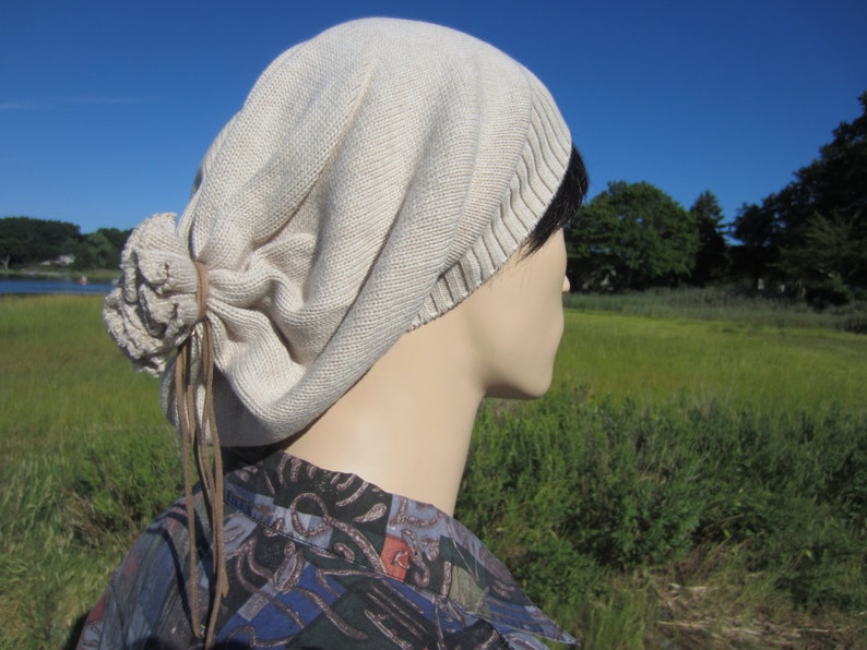 May include: A beige slouchy beanie with a brown leather tie. The beanie is made of a soft, knitted fabric and has a relaxed, casual look.