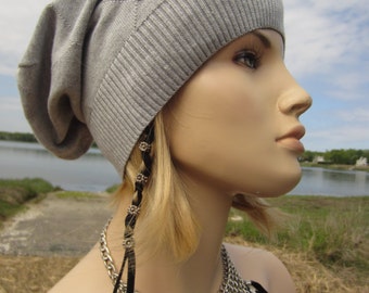 Può includere: Un berretto grigio soffice con un design a stella e strass. Il berretto è indossato da una persona con i capelli lunghi e biondi e una collana a catena argentata con nappe nere.