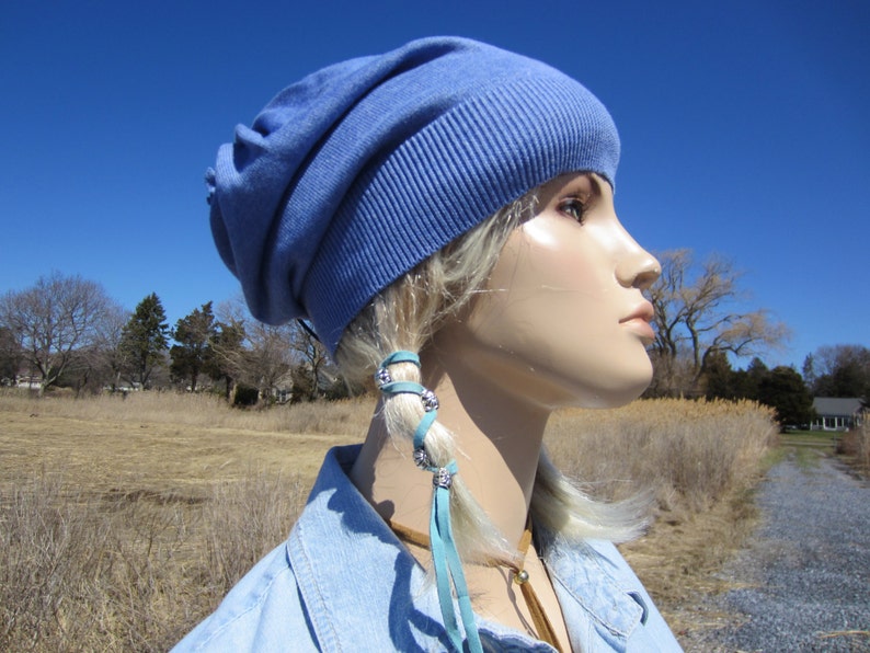 May include: A blue slouchy beanie with a light blue leather hair tie with silver accents. The hair tie is tied around a braid of blonde hair.