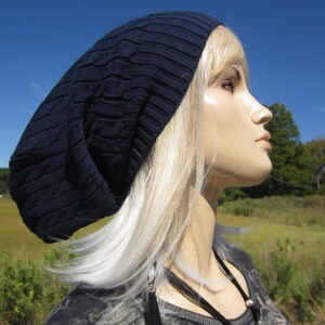 Puede incluir: Un gorro azul marino con un patr&oacute;n de punto de cable. El gorro lo lleva una persona con el pelo largo y rubio.