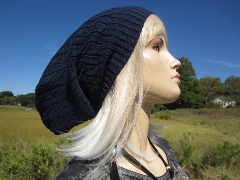 Puede incluir: Un gorro azul marino con un patr&oacute;n de punto de cable. El gorro lo lleva una persona con el pelo largo y rubio.