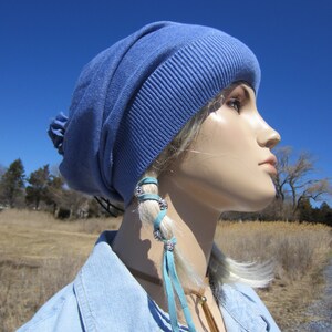 May include: A blue beanie with a light blue leather cord tied around the top. The cord has silver beads and is tied in a knot at the end. The beanie is worn by a mannequin with a blue denim shirt.