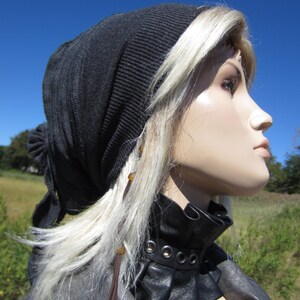 May include: A black beanie with a long, flowing blonde wig. The wig is styled with brown leather cords and beads. The person is wearing a black leather choker with a ruffled edge and silver eyelets.