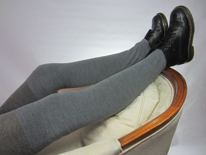 K&ouml;nnte beinhalten: Schwarze Lederstiefel mit Schn&uuml;rung und graue Leggings. Die Leggings sind einfarbig, mit einem dunkleren Graubereich am Knie. Die Stiefel werden beim Entspannen in einem Stuhl getragen.