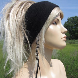May include: A woman with blonde hair is wearing a black headband and a silver beaded hair tie. The hair tie is attached to a black cord.