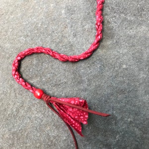 May include: A red braided fabric hair tie with white polka dots and a red bead accent. The hair tie has a black plastic clip at the top.