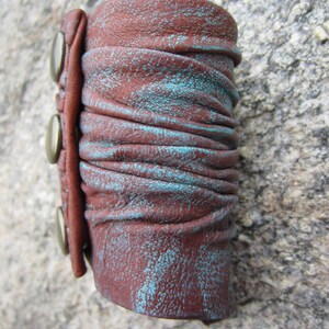 May include: A brown leather cuff bracelet with turquoise accents and three silver metal snaps.