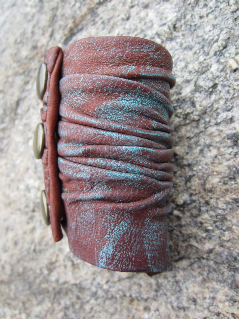 May include: A brown leather cuff bracelet with turquoise accents and three silver metal snaps.