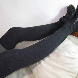 K&ouml;nnte beinhalten: Dunkelgraue Overknee-Socken mit einem hellgrauen Band, kombiniert mit schwarzen Lederstiefeln. Die Stiefel haben gelbe N&auml;hte und Schn&uuml;rsenkel. Die Socken sind &uuml;ber die Stiefel gezogen.