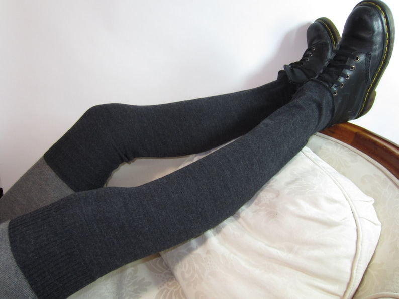 K&ouml;nnte beinhalten: Dunkelgraue Overknee-Socken mit einem hellgrauen Band, kombiniert mit schwarzen Lederstiefeln. Die Stiefel haben gelbe N&auml;hte und Schn&uuml;rsenkel. Die Socken sind &uuml;ber die Stiefel gezogen.