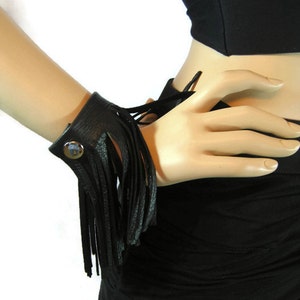 May include: A black leather cuff bracelet with a fringe detail. The bracelet has a snap closure and a decorative metal button.