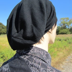 K&ouml;nnte beinhalten: Eine schwarze M&uuml;tze aus weichem, gestricktem Stoff. Die M&uuml;tze ist nach unten gefaltet und wird auf dem Kopf getragen. Die M&uuml;tze wird von einer Person mit kurzen, dunklen Haaren getragen.