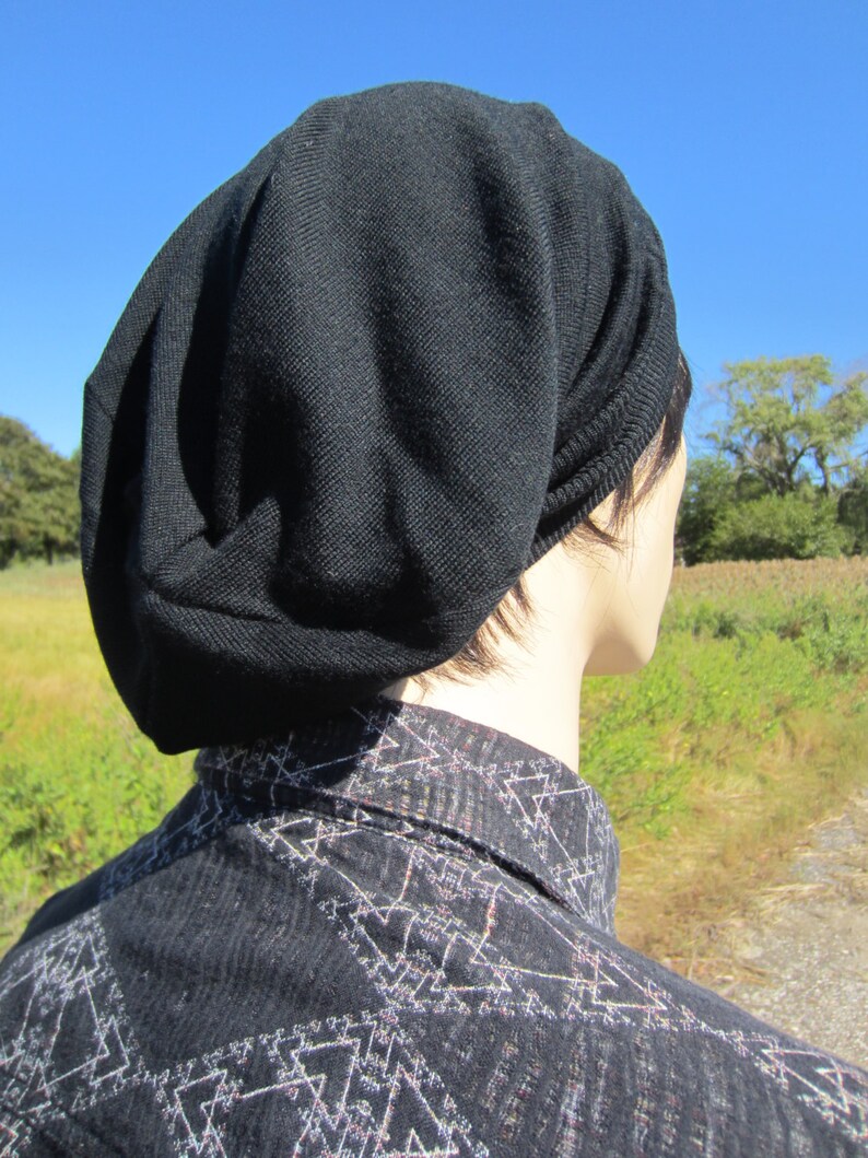 K&ouml;nnte beinhalten: Eine schwarze M&uuml;tze aus weichem, gestricktem Stoff. Die M&uuml;tze ist nach unten gefaltet und wird auf dem Kopf getragen. Die M&uuml;tze wird von einer Person mit kurzen, dunklen Haaren getragen.