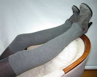 Könnte beinhalten: Graue gestrickte Oberschenkelsocken mit einem Paar grauen Wildlederstiefeln mit Absatz. Die Socken werden über schwarzen Strumpfhosen getragen und die Stiefel ruhen auf einem weißen Sessel.