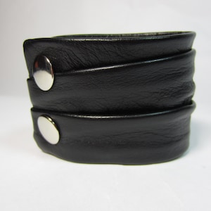 May include: A black leather cuff bracelet with two silver snaps.