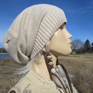 May include: A beige slouchy beanie hat with a long, white braid with brown beads hanging from the side.