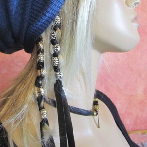 May include: Black leather hair ties with silver beads, worn in a woman's blonde hair. The hair ties are tied in two separate strands of hair, with the ends of the ties hanging down.