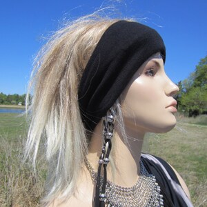 May include: A person with long, blonde hair wearing a black headband and a silver necklace with a beaded pendant. The person is looking to the right and has a neutral expression.