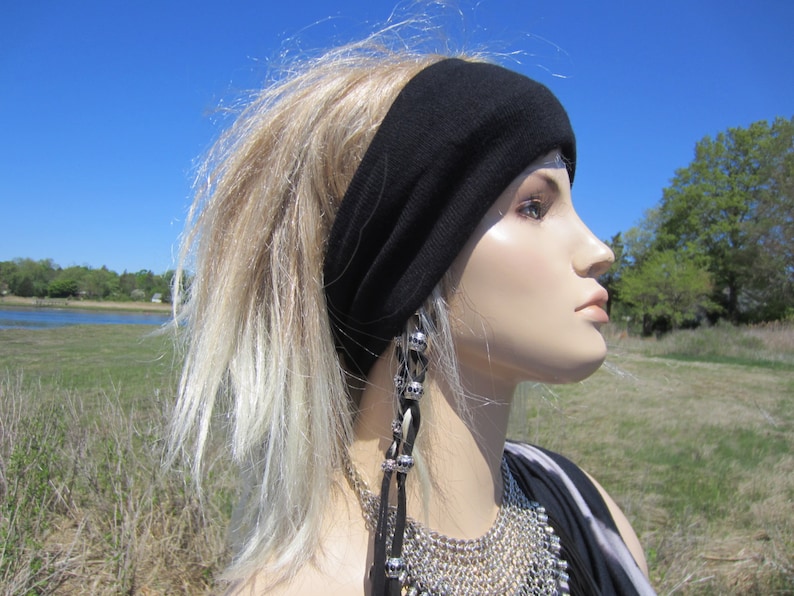 May include: A person with long, blonde hair wearing a black headband and a silver necklace with a beaded pendant. The person is looking to the right and has a neutral expression.