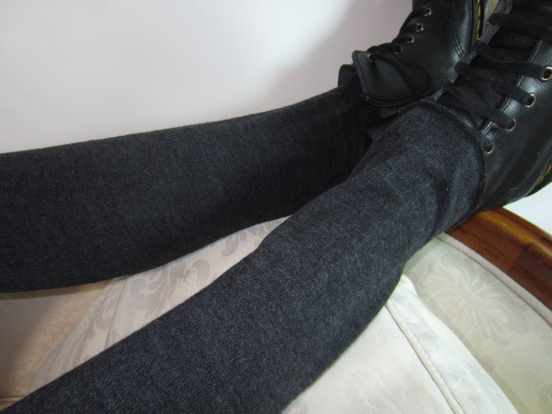 K&ouml;nnte beinhalten: Dunkelgraue Leggings kombiniert mit schwarzen Lederstiefeln. Die Leggings sind einfarbig und scheinen aus einem weichen Strickstoff zu bestehen. Die Stiefel haben Schn&uuml;rsenkel und ein klassisches Design.