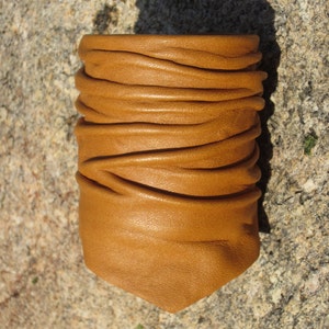 May include: A brown leather bracelet with a folded design. The bracelet is made of soft, supple leather and has a natural, rustic look.