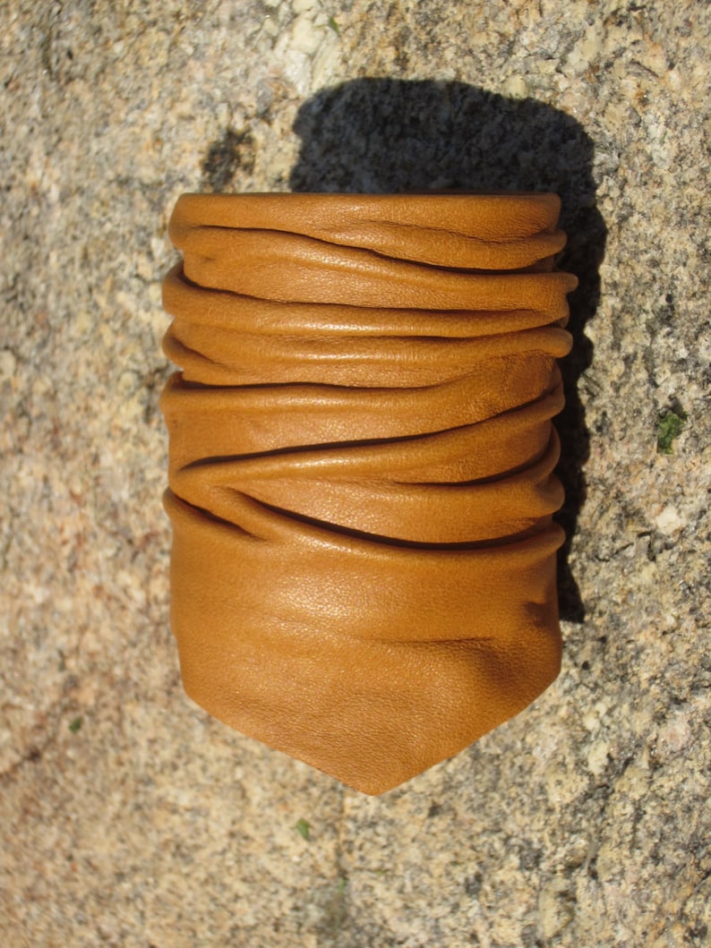 May include: A brown leather bracelet with a folded design. The bracelet is made of soft, supple leather and has a natural, rustic look.