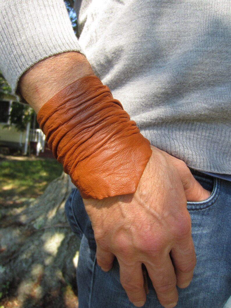 May include: A brown leather bracelet wrapped around a person's wrist. The bracelet is made of multiple layers of leather and has a slightly textured surface.