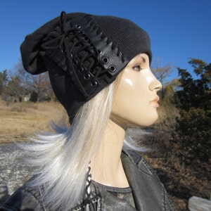 May include: A black beanie with a leather lace detail. The beanie is made of a soft, knit fabric and has a slouchy fit.