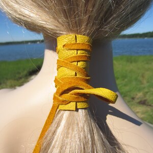May include: A yellow leather ponytail holder tied around a ponytail of blonde hair.