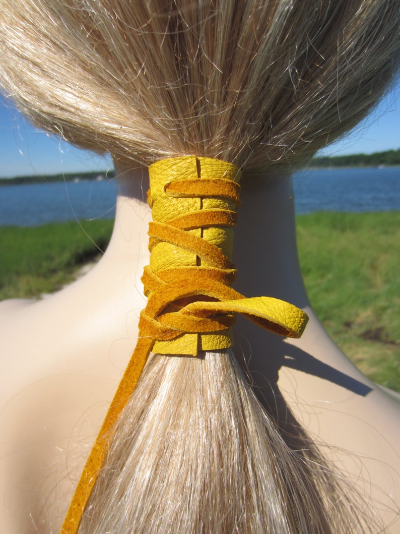 May include: A yellow leather ponytail holder tied around a ponytail of blonde hair.