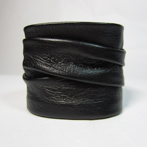 May include: A black leather cuff bracelet with a folded design. The bracelet is made of soft, supple leather and has a simple, elegant look.