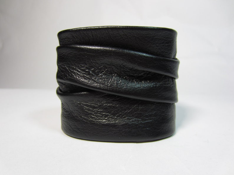May include: A black leather cuff bracelet with a folded design. The bracelet is made of soft, supple leather and has a simple, elegant look.